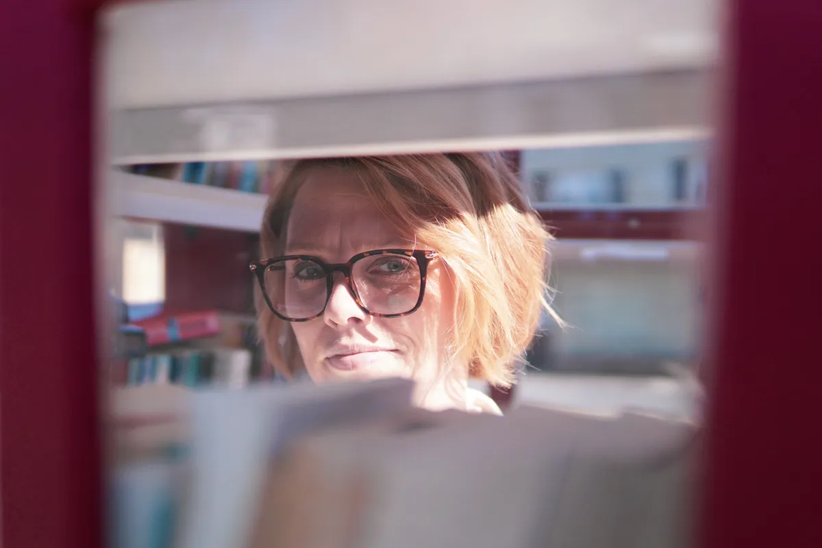 my wife looking at me through the glass from inside a British telephone box that has been turned into a little library