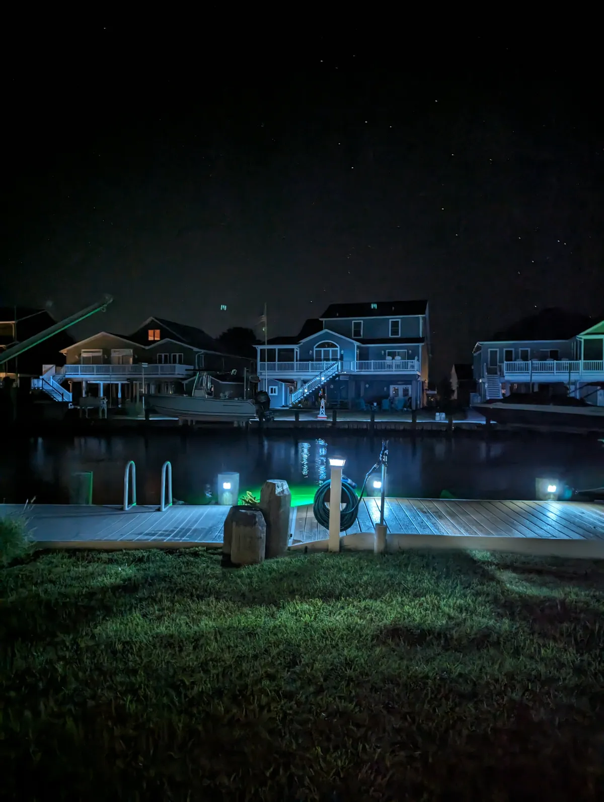 A night photo of the canal at my in-laws' house on the Virginia eastern shore. The photo is lit by lights on the walkway and houses. Stars can be seen in the sky.